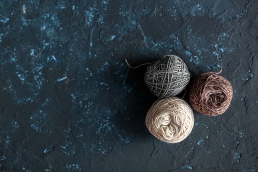 three beige gray brown Color balls skein of wool yarn for crochet and knit on dark blue texture putty concrete. Flatlay image with space for text.