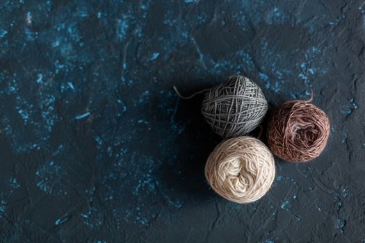 three beige gray brown Color balls skein of wool yarn for crochet and knit on dark blue texture putty concrete. Flatlay image with space for text.