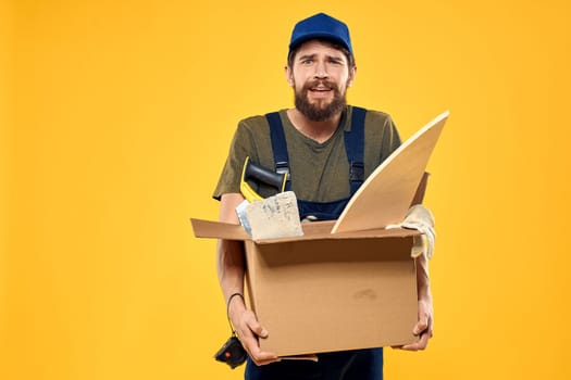 A man in a working form a box with loading tools yellow background. High quality photo