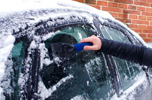 Cleaning snow from windshield. Winter vehicle front windows clean. Woman scraping ice from the windshield of a car. Winter driving. Woman removing snow from automobile. Cold snowy and frosty morning.