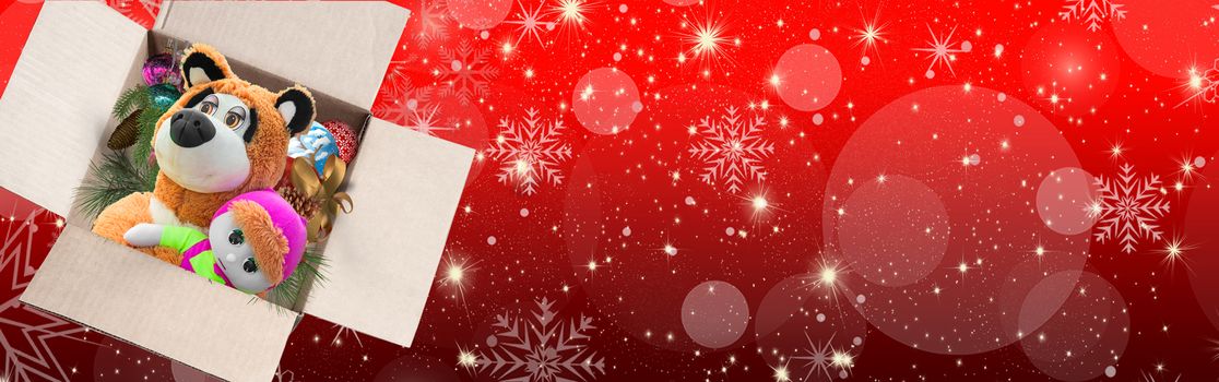 An open box with toys and Christmas decorations on a beautiful red background with bokeh and snowflakes, a Christmas gift for children. Greeting card, banner.