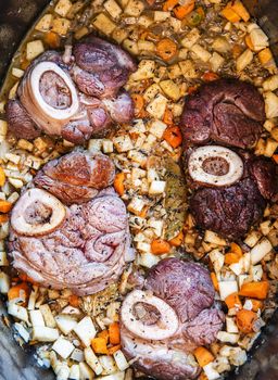 Osso buco in bianco is traditional Italain dish from the Milan area. The veal meat slices with marrow bone are being cooked in a large casserole along with root vegetables, spice and wine sauce