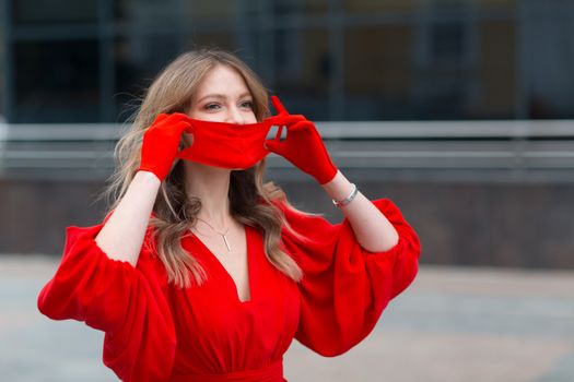 Young woman in red dress and gloves puts on medical face mask.