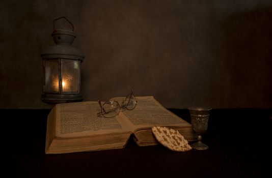 a still life of a bible with an old pewter lamp with a tea light burning with an old bible and supper