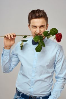 Romantic man with a red rose and in a blue shirt with a bow tie around his neck gray background. High quality photo