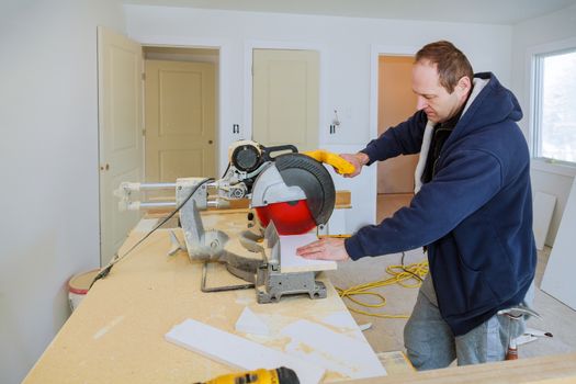 Builder uses circular saw tool to cut wood baseboard woodwork equipment