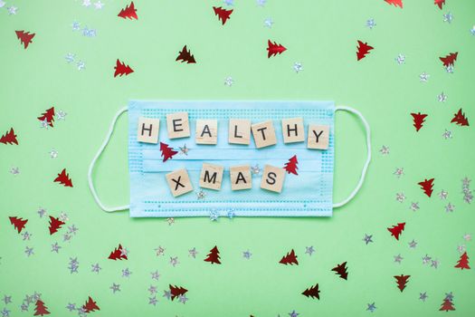 inscription from wooden blocks of a healthy xmas on a medical protective mask and on a new year background
