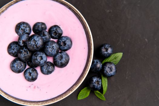 Tasty fresh blueberry yoghurt shake dessert in ceramic bowl standing on black table background. Homemade berry smoothie. Healthy eating. Diet food. yogurt