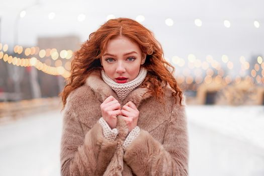 Young beautiful redhead girl freckles ice rink background Pretty woman curly hair portrait walking new year fair Modern cute female frozen in the cold chrismas holiday decorated street.