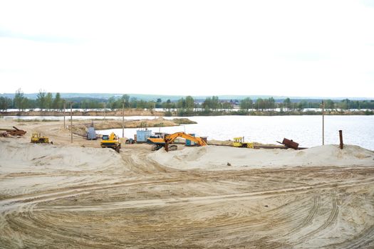 Sand quarry mining industry equipment excavator tractor standing sand land near lake water Industrial activity mine operation summer sunny day. Ecology problem Non-renewable resources of the Earth