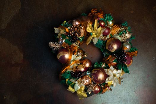 Christmas wreath on brown background with copyspace. Wreath decorated with balls and bows of gold and brown, with green leaves. Luxury New Year decor