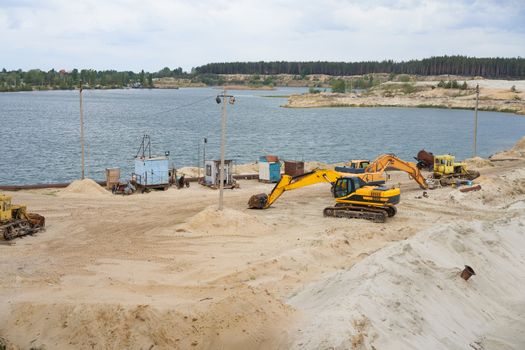 Sand quarry mining industry equipment excavator tractor standing sand land near lake water Industrial activity mine operation summer sunny day. Ecology problem Non-renewable resources of the Earth
