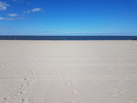 beach with tire tracks and foot prints and ocean water and blue sky