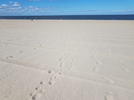 beach with tire tracks and foot prints and ocean water and blue sky