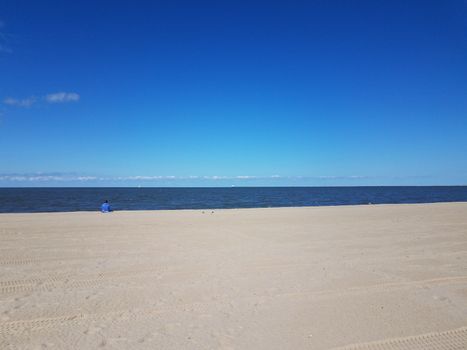 beach with tire tracks and foot prints and ocean water and blue sky