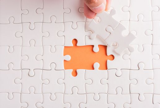 Top view flat lay of hand-holding last piece white paper jigsaw puzzle game last pieces put to place for solve problem complete mission, studio shot on an orange background, quiz calculation concept