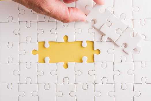 Top view flat lay of hand-holding last piece white paper jigsaw puzzle game last pieces put to place for solve problem complete mission, studio shot on a yellow background, quiz calculation concept
