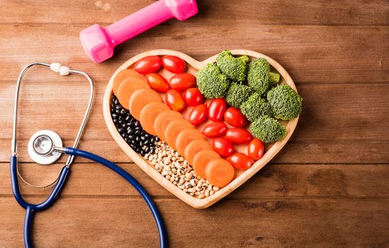 Top view of fresh organic fruits and vegetables in heart plate wood (carrot, Broccoli, tomato), doctor stethoscope and sport dumbbell on wooden table, Healthy lifestyle diet food concept