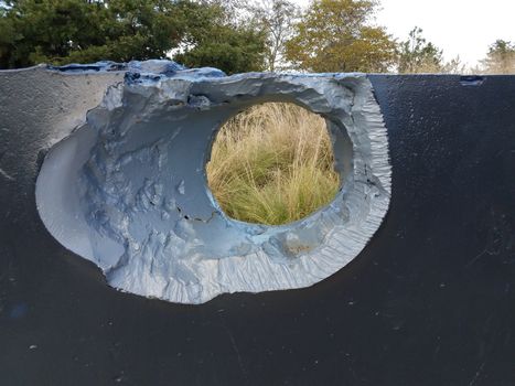large hole or damage in metal wall with trees