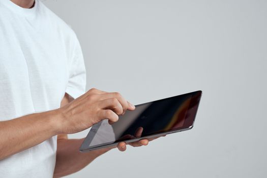 Tablet with a touch screen on a light background male hands white t-shirt cropped view. High quality photo