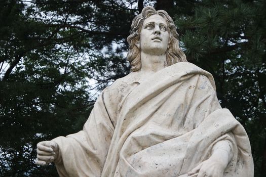 Statue of a man holding a book in one hand. White marble statue of man in a public park