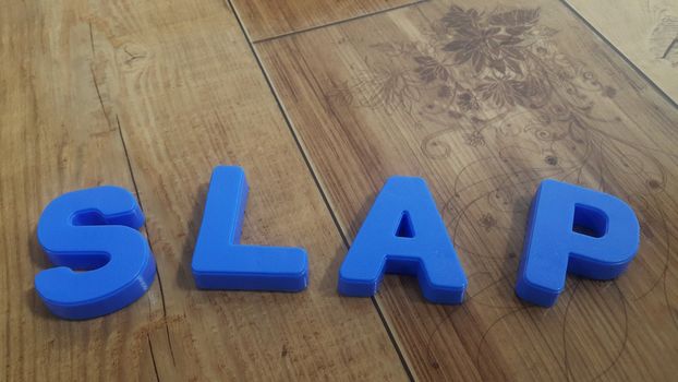 Plastic colored alphabets making words are placed on a wooden floor. These plastic letters can be used for teaching kids.