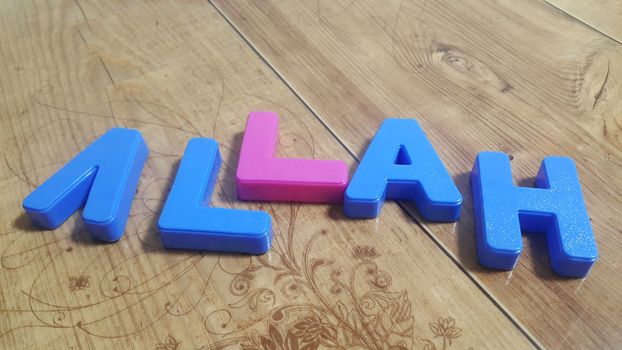 Plastic colored alphabets making words are placed on a wooden floor. These plastic letters can be used for teaching kids.