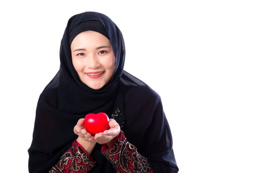 Portrait of young asian muslim woman holding red heart shaped pillow isolated on white background.