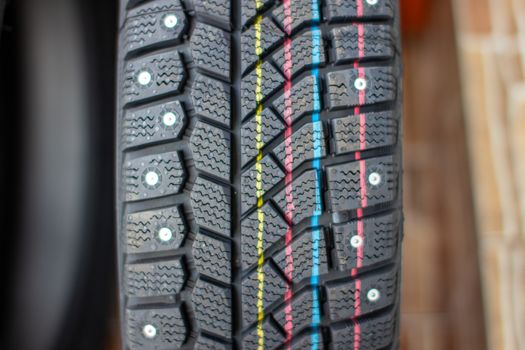 New, black winter car tires with spikes. Safe driving, preparing for winter. Tires with yellow, blue and red stripes