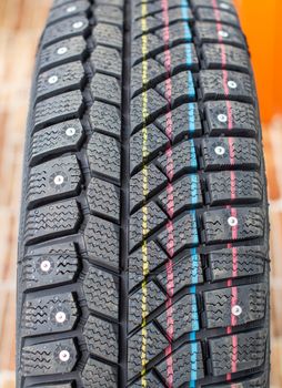 New, black winter car tires with spikes. Safe driving, preparing for winter. Tires with yellow, blue and red stripes