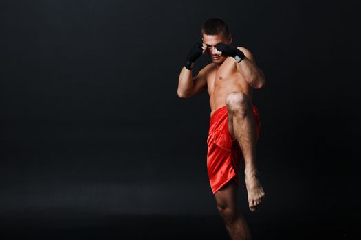 Sportsman muay thai man boxer stance ad knee kick at black background.