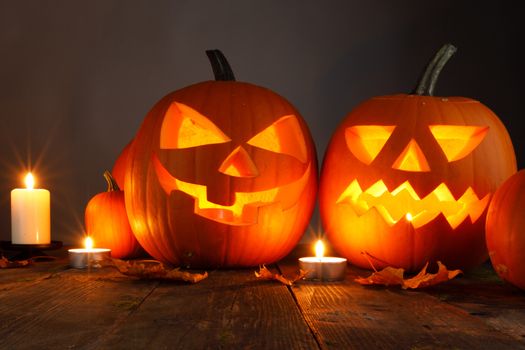 Halloween pumpkin head lanterns and burning candles on wooden background