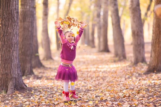 Cute little girl in autumn park with orange and yellow color leaves.