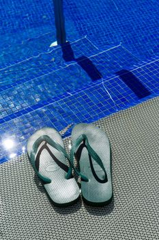 A pair of green flip-flops at the entrance to a pool