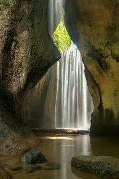 Beautiful secret Tukad Cepung Waterfall in Bali, Indonesia. Long exposure shot. Rays of sun are shining through the mountain over the waterfall. Famous hidden waterfall between rocks. Romantic place.