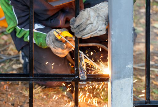 A welder using an electrode welds a metal fence in an autumn park, bright sparks fly, selective focus, copy space.