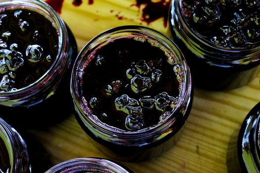 The process of filling homemade chokeberry jam on a tray. Jars full of chokeberry jam, ready to close. Aronia. Zavidovici, Bosnia and Herzegovina.