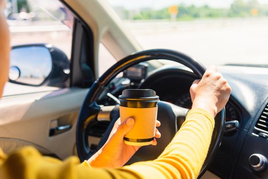 Asian woman drinking hot coffee takeaway cup inside a car and while driving the car in the morning during going to work on highway, Transportation and vehicle concept