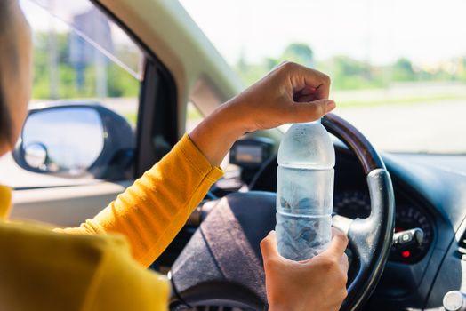 Asian woman holding a water bottle for drink while driving the car in the morning during going to work on highway road, Transportation and vehicle concept