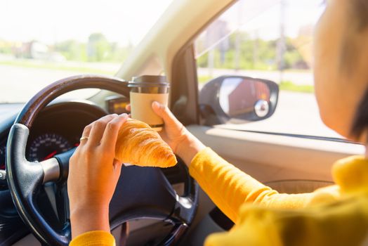 Asian woman eating food fastfood and drink coffee while driving the car in the morning during going to work on highway road, Transportation and vehicle concept