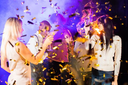 Having fun together. Group of beautiful young happy multi race people dance holding champagne in golden confetti and smiling nightlife new year celebration party