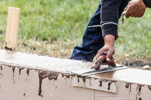 Construction Worker Using Wood Trowel On Wet Cement Forming Coping Around New Pool.