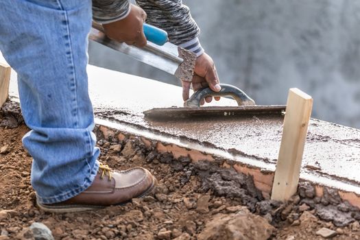 Construction Worker Using Wood Trowel On Wet Cement Forming Coping Around New Pool.