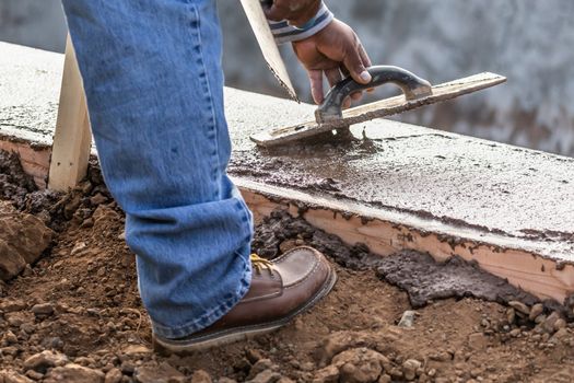 Construction Worker Using Wood Trowel On Wet Cement Forming Coping Around New Pool.