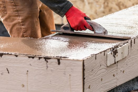 Construction Worker Using Wood Trowel On Wet Cement Forming Coping Around New Pool.