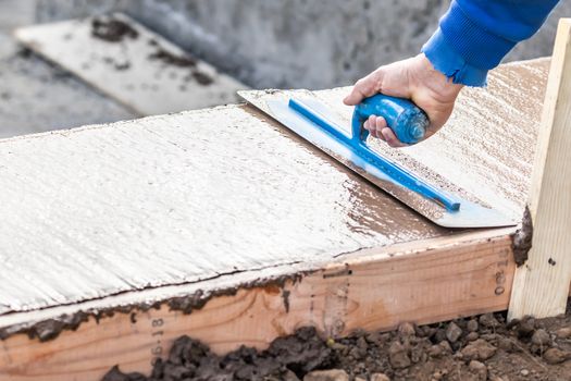 Construction Worker Using Trowel On Wet Cement Forming Coping Around New Pool.