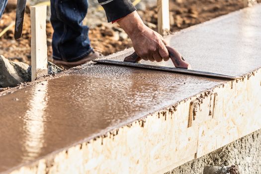 Construction Worker Using Wood Trowel On Wet Cement Forming Coping Around New Pool.