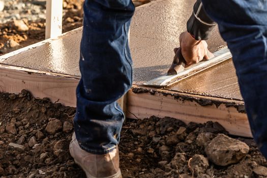 Construction Worker Using Wood Trowel On Wet Cement Forming Coping Around New Pool.