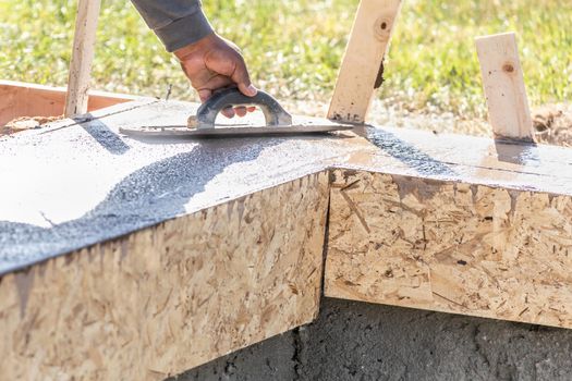 Construction Worker Using Wood Trowel On Wet Cement Forming Coping Around New Pool.