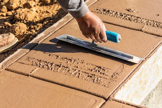 Construction Worker Using Trowel On Wet Cement Forming Coping Around New Pool.